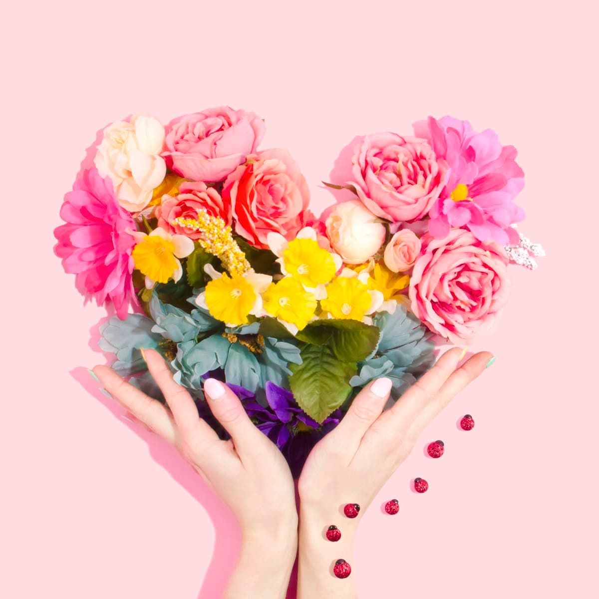 Hands holding a heart-shaped arrangement of fresh pink roses and yellow flowers